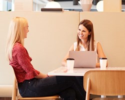 Two female professionals meeting over a coffee in an office