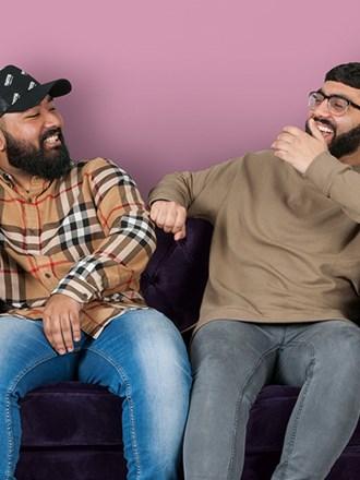 2 men sitting on purple sofa laughing