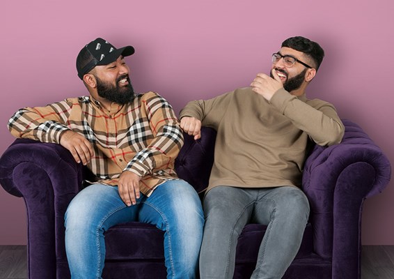 2 men sitting on purple sofa laughing